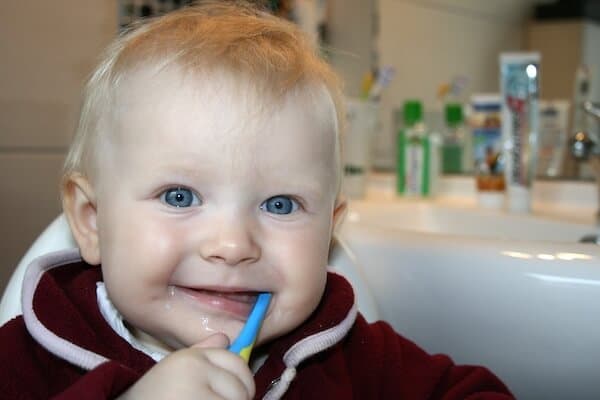 First Dentist Visit At What Age - a smiling young baby chews on a toothbrush.